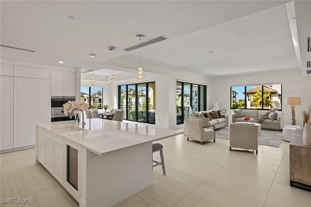 kitchen with sink, pendant lighting, a breakfast bar area, a center island with sink, and white cabinets