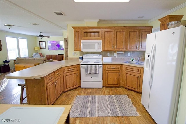 kitchen featuring kitchen peninsula, white appliances, ceiling fan, sink, and a breakfast bar area