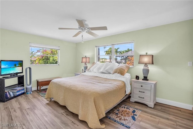 bedroom featuring ceiling fan, light hardwood / wood-style floors, and multiple windows