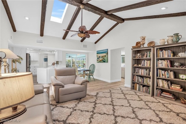 living room featuring light wood-type flooring, a skylight, ceiling fan, beam ceiling, and high vaulted ceiling