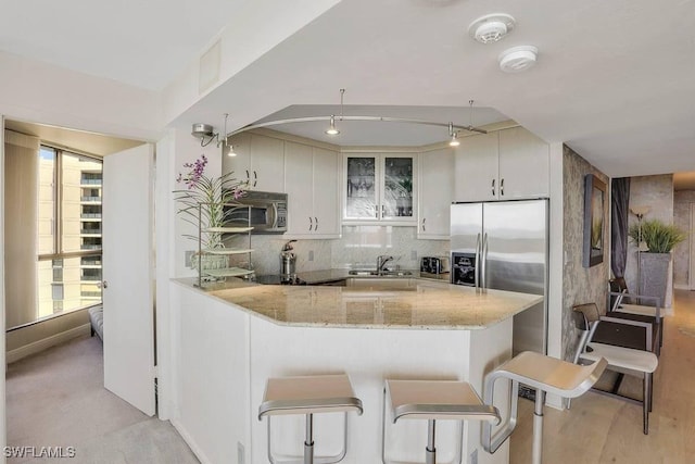 kitchen featuring white cabinetry, light stone countertops, stainless steel appliances, kitchen peninsula, and a breakfast bar