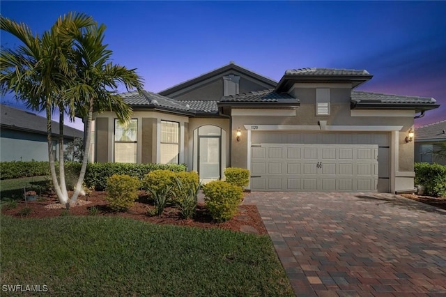 view of front of house with a garage, a tiled roof, decorative driveway, and stucco siding