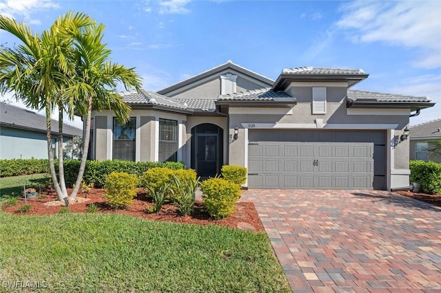 view of front of property featuring stucco siding, a tile roof, an attached garage, decorative driveway, and a front yard