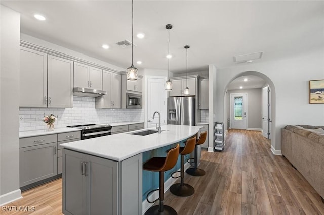 kitchen featuring arched walkways, gray cabinets, stainless steel appliances, under cabinet range hood, and a sink