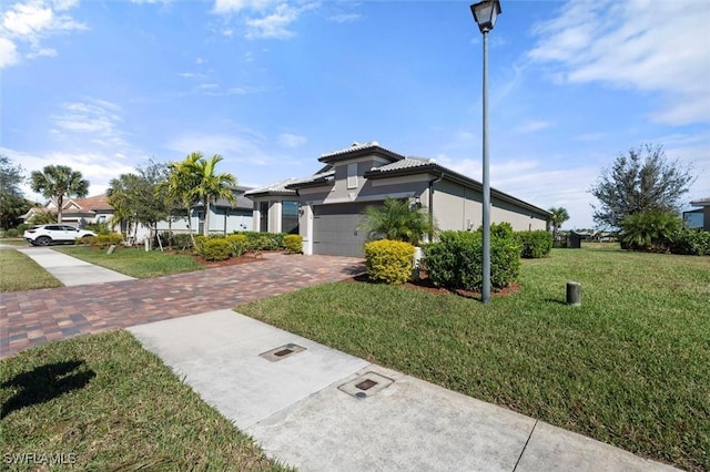 view of front of home featuring a tiled roof, an attached garage, decorative driveway, a front yard, and stucco siding