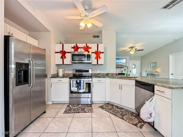 kitchen with dark stone counters, kitchen peninsula, light tile patterned floors, appliances with stainless steel finishes, and white cabinetry