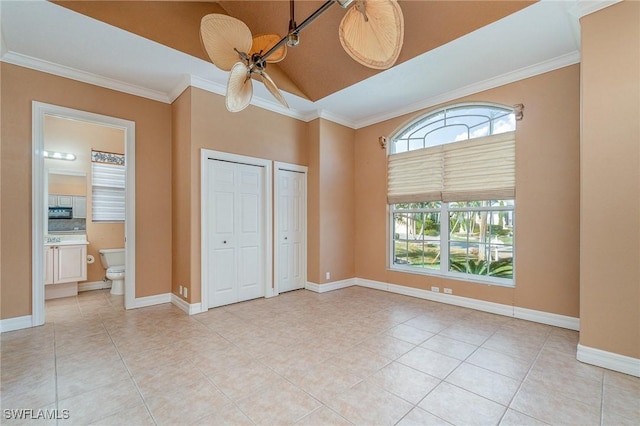 unfurnished bedroom featuring connected bathroom, ceiling fan, crown molding, and two closets