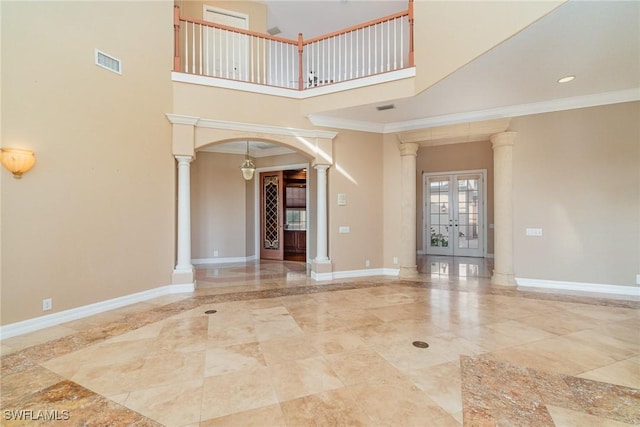 unfurnished living room featuring french doors, a towering ceiling, decorative columns, and ornamental molding