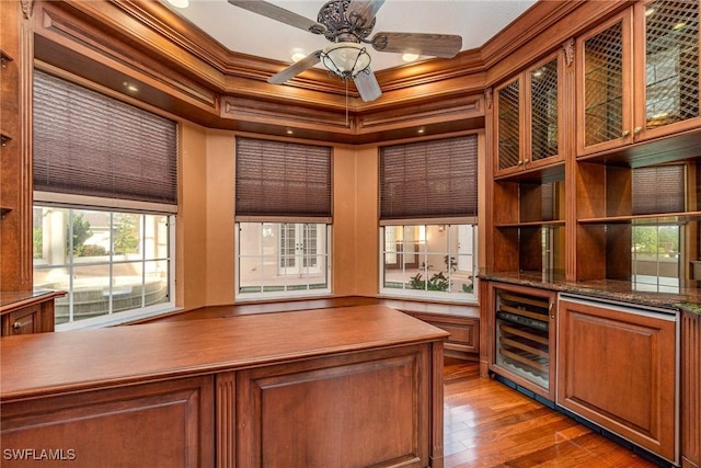 unfurnished office with light wood-type flooring, beverage cooler, ornamental molding, and ceiling fan