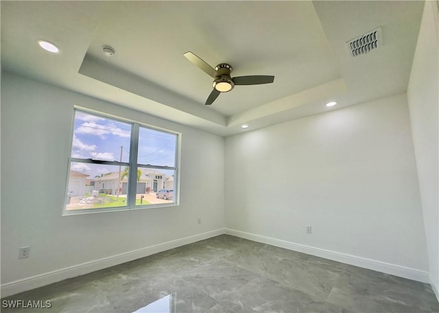 empty room with ceiling fan and a raised ceiling