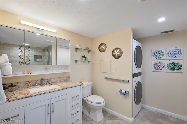 bathroom with a tile shower, vanity, stacked washing maching and dryer, and toilet