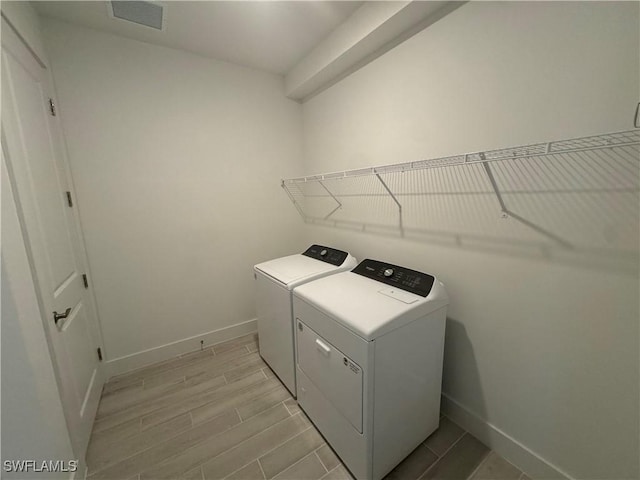 clothes washing area featuring wood finish floors, washer and clothes dryer, visible vents, laundry area, and baseboards