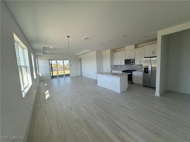 kitchen featuring stainless steel appliances, a kitchen island with sink, decorative light fixtures, white cabinets, and light hardwood / wood-style floors