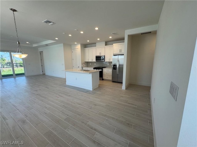 kitchen featuring visible vents, open floor plan, a sink, stainless steel appliances, and backsplash