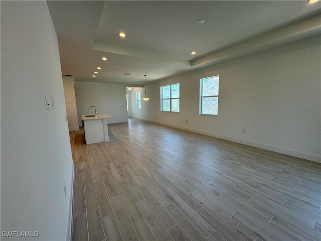 empty room featuring light wood-style flooring, recessed lighting, a sink, baseboards, and a tray ceiling