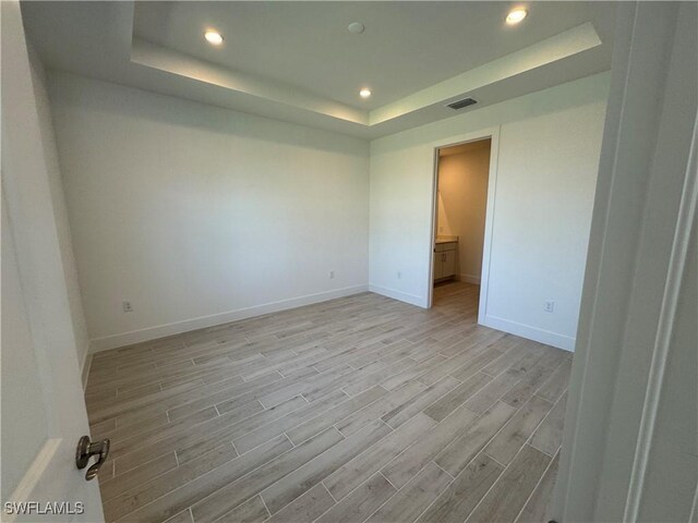 empty room featuring visible vents, a raised ceiling, baseboards, wood tiled floor, and recessed lighting