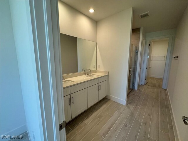 bathroom with a sink, baseboards, a spacious closet, a shower stall, and wood tiled floor