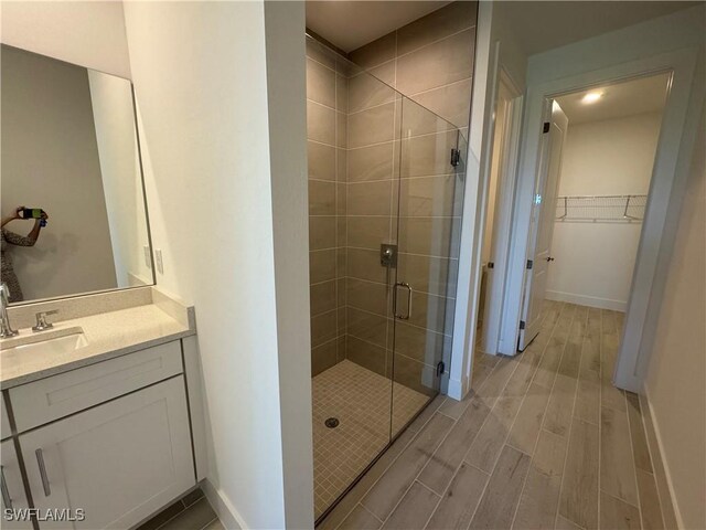 full bathroom with a stall shower, a spacious closet, vanity, and wood finish floors