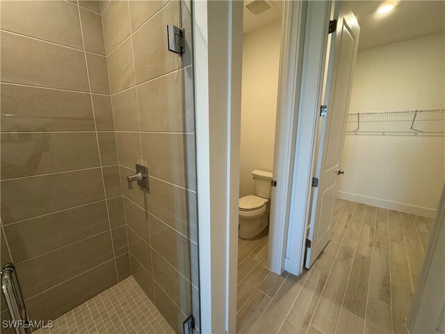 bathroom with a walk in closet, toilet, a shower stall, wood finished floors, and baseboards