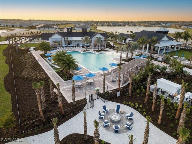 pool at dusk with a residential view, a patio area, fence, and a community pool