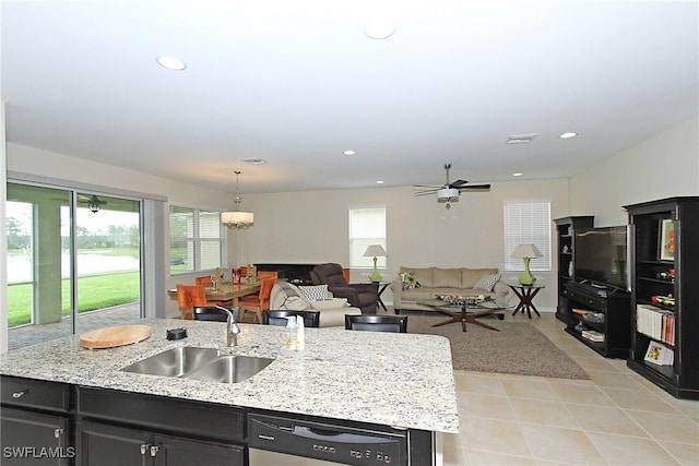 kitchen featuring a kitchen island with sink, sink, stainless steel dishwasher, light stone countertops, and decorative light fixtures