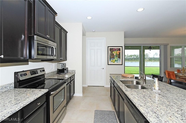 kitchen with a water view, sink, light stone countertops, light tile patterned floors, and stainless steel appliances