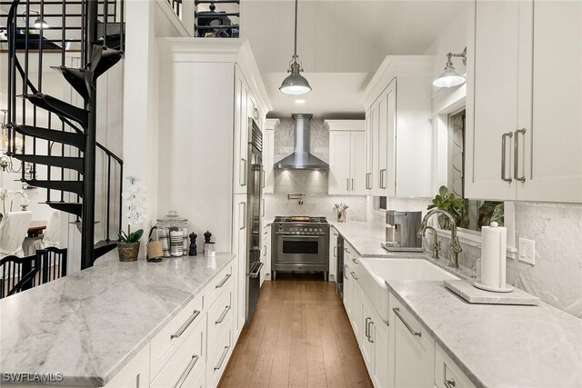 kitchen with sink, high end stove, light stone countertops, white cabinets, and wall chimney exhaust hood