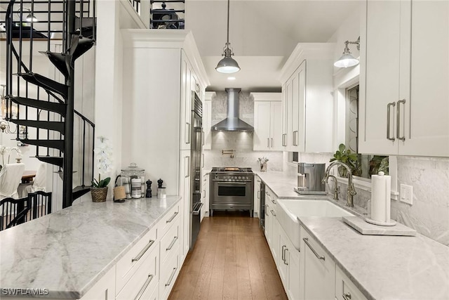 kitchen with a sink, white cabinets, wall chimney range hood, high end stainless steel range oven, and decorative backsplash