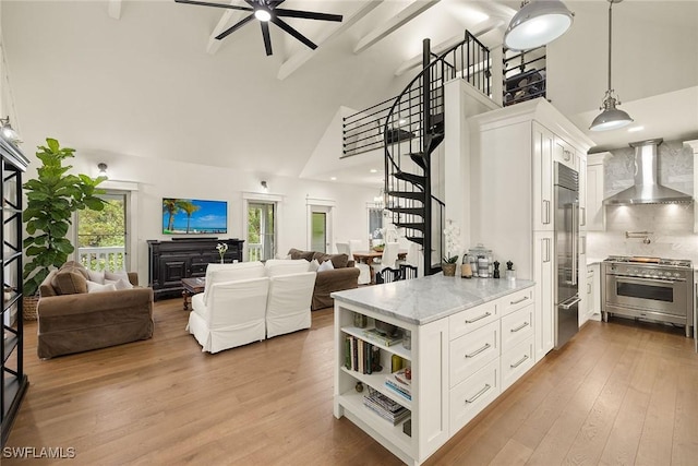 kitchen with wood finished floors, high end stainless steel range oven, wall chimney range hood, a fireplace, and white cabinetry