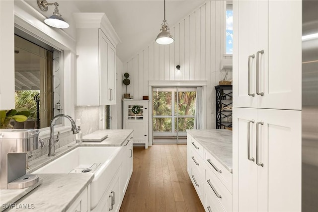 kitchen featuring wood-type flooring, hanging light fixtures, white cabinetry, a sink, and light stone countertops