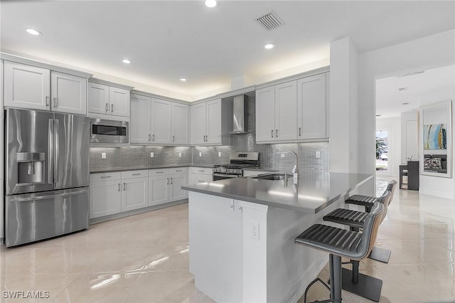 kitchen with sink, a breakfast bar area, kitchen peninsula, stainless steel appliances, and wall chimney exhaust hood