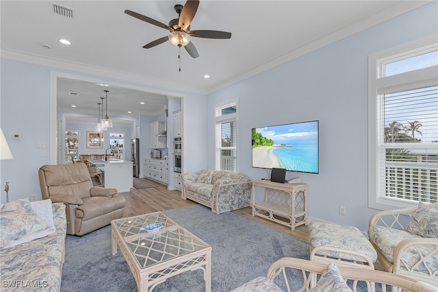 living room with a wealth of natural light, light wood-type flooring, ceiling fan, and ornamental molding