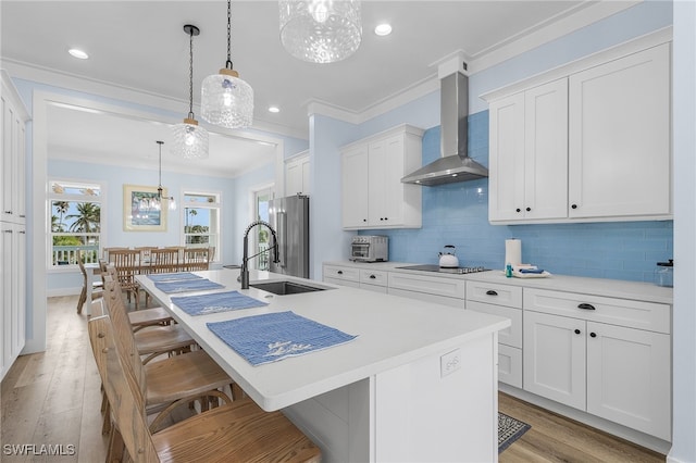 kitchen featuring a kitchen island with sink, wall chimney exhaust hood, and hanging light fixtures