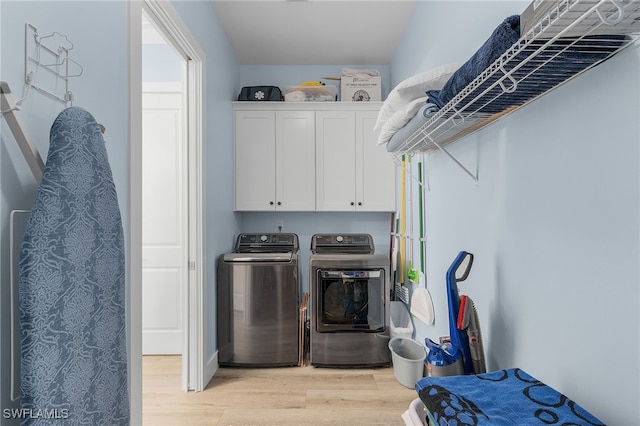 clothes washing area featuring washer and clothes dryer, cabinets, and light wood-type flooring