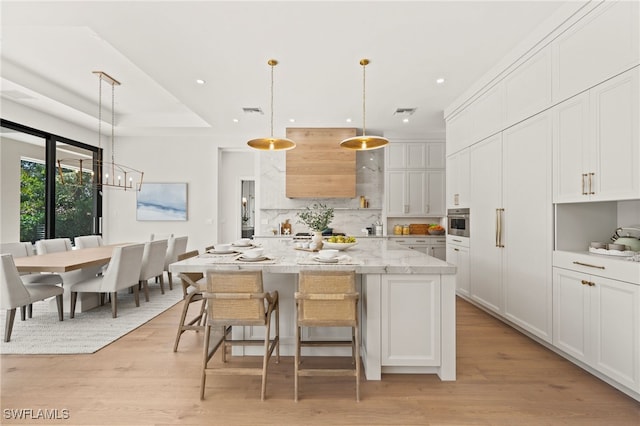 kitchen with stainless steel oven, pendant lighting, light stone countertops, a kitchen island with sink, and white cabinets