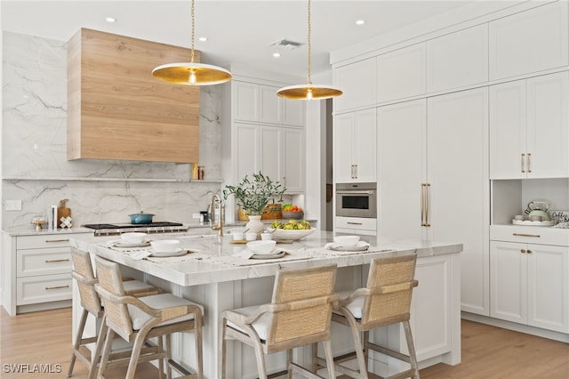 kitchen featuring white cabinetry, pendant lighting, a center island with sink, and light stone counters