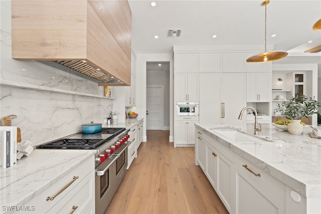 kitchen featuring sink, custom exhaust hood, white cabinetry, decorative light fixtures, and range with two ovens