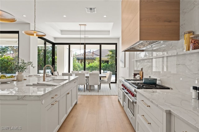 kitchen with white cabinetry, hanging light fixtures, a tray ceiling, light stone countertops, and range with two ovens