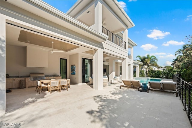 view of patio / terrace featuring exterior kitchen, area for grilling, a balcony, ceiling fan, and a fenced in pool