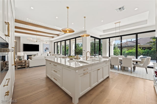 kitchen with decorative light fixtures, white cabinetry, an island with sink, sink, and light stone counters