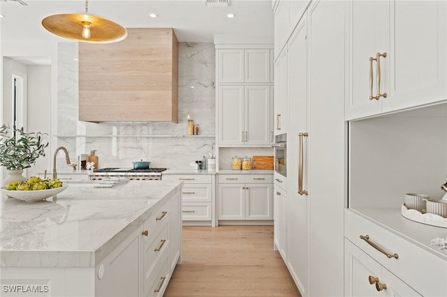 kitchen with white cabinets, hanging light fixtures, light hardwood / wood-style floors, light stone counters, and stainless steel appliances