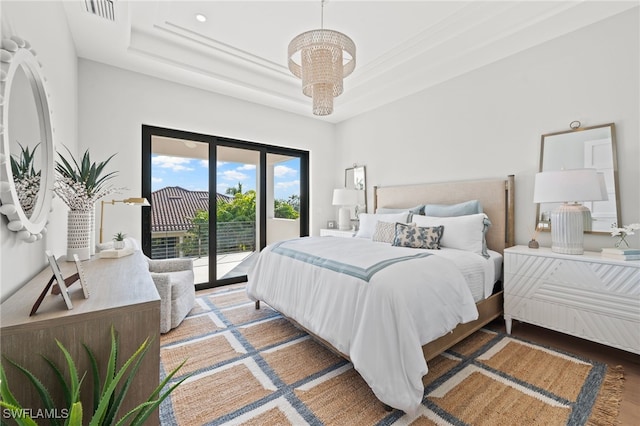 bedroom featuring a notable chandelier, a raised ceiling, wood-type flooring, and access to exterior