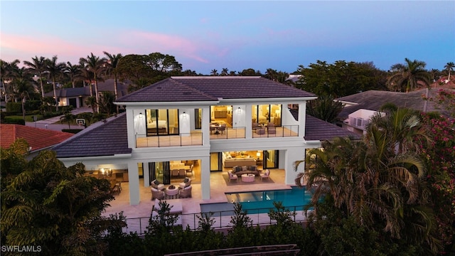 back house at dusk with outdoor lounge area, a patio, and a balcony