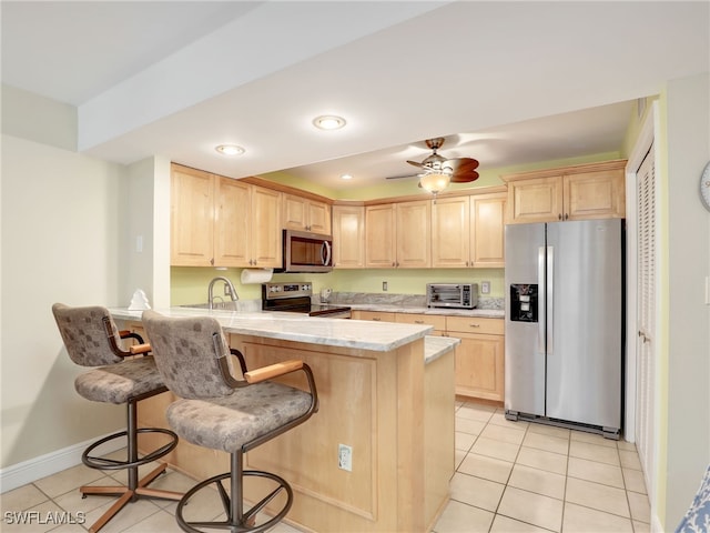 kitchen with stainless steel appliances, a kitchen breakfast bar, kitchen peninsula, light brown cabinetry, and light tile patterned floors