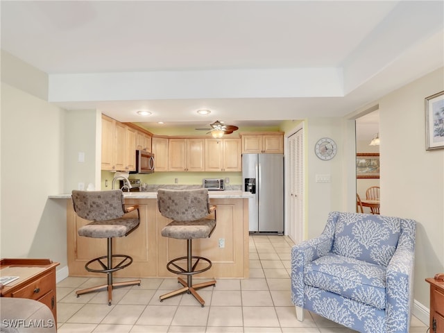 kitchen with light brown cabinets, stainless steel appliances, a kitchen breakfast bar, kitchen peninsula, and light tile patterned floors