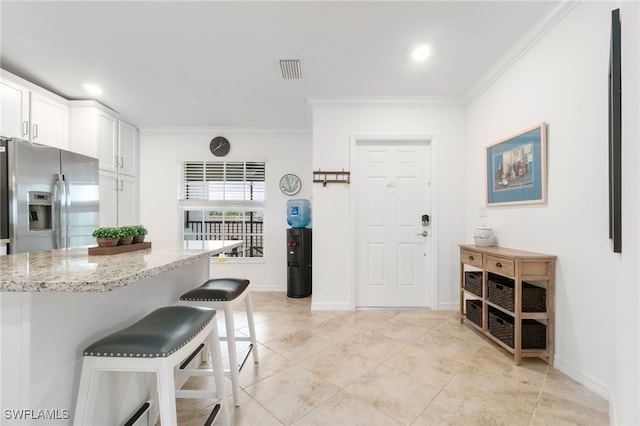 kitchen featuring light stone counters, stainless steel fridge, crown molding, a kitchen bar, and white cabinets