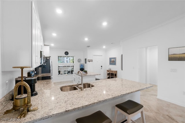 kitchen featuring sink, light stone countertops, ornamental molding, a kitchen bar, and white cabinetry