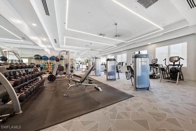 gym with a raised ceiling and light carpet