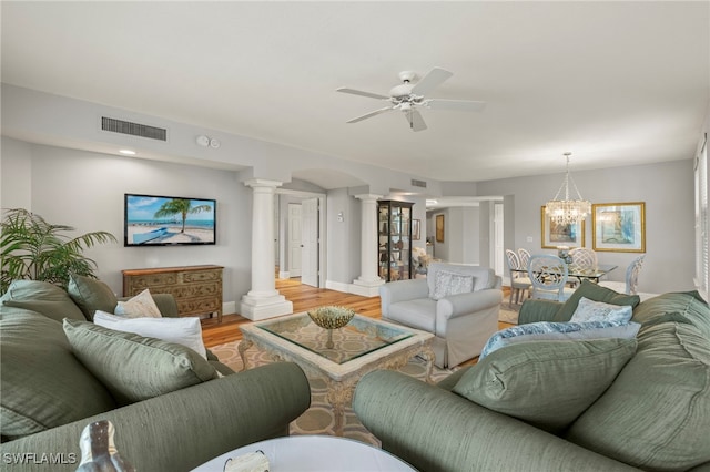 living room featuring ceiling fan with notable chandelier, wood-type flooring, and ornate columns