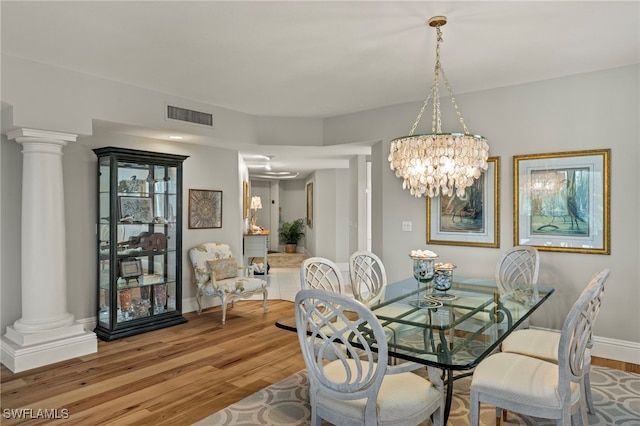 dining space featuring ornate columns, wood-type flooring, and an inviting chandelier